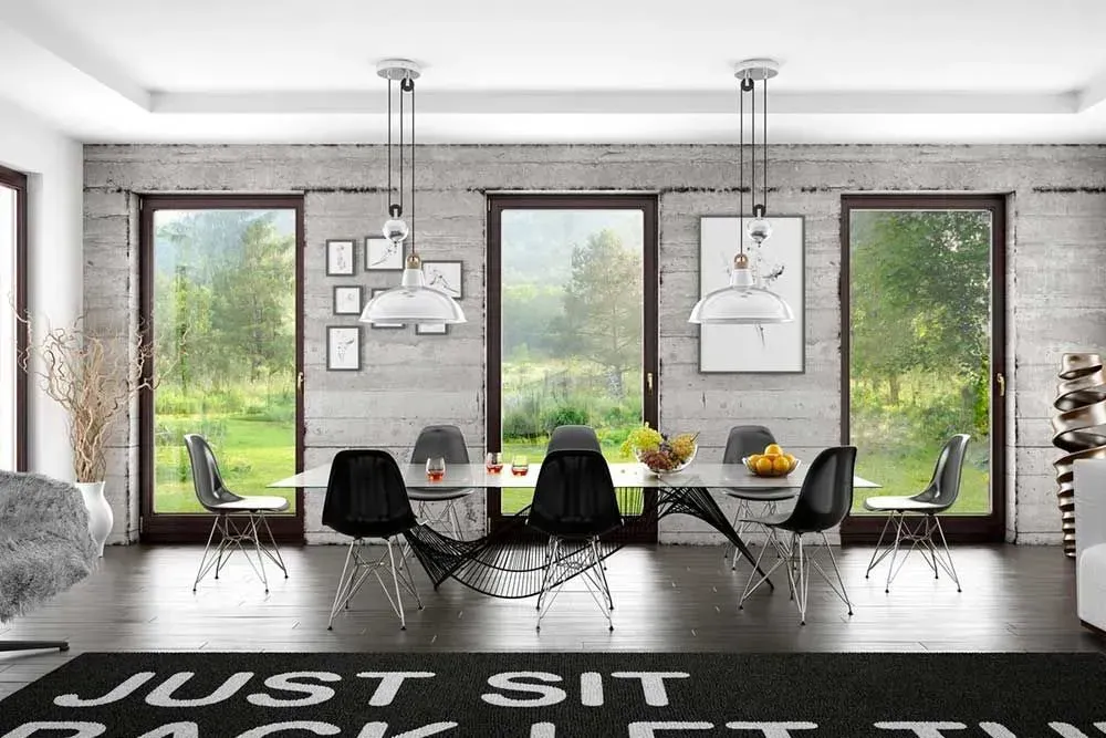 Sala da pranzo moderna con ampie finestre, sedie nere, lampade a sospensione e un lungo tavolo con centrotavola di frutta.