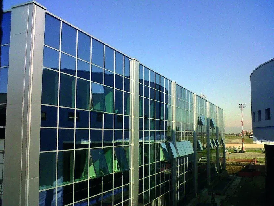 Moderno edificio per uffici in vetro con vetrate riflettenti sotto un cielo azzurro limpido.