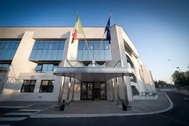 Ingresso di un moderno edificio per uffici con facciata in vetro e due bandiere sopra la tettoia.