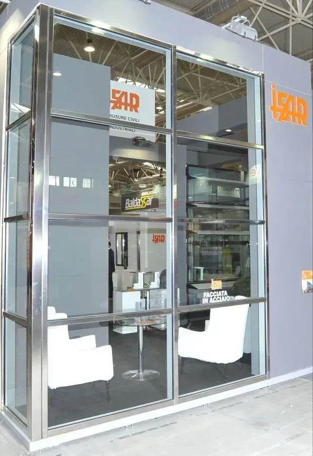 Cabina da ufficio con frontale in vetro, sedie bianche e tavolo all'interno di una parete grigia