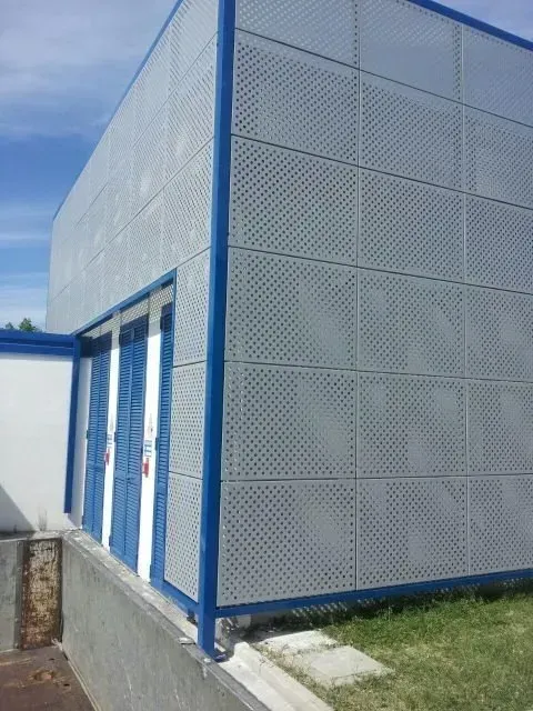 Edificio di servizio blu e bianco con rivestimento in rete metallica e porte chiuse, adiacente a un sentiero erboso.
