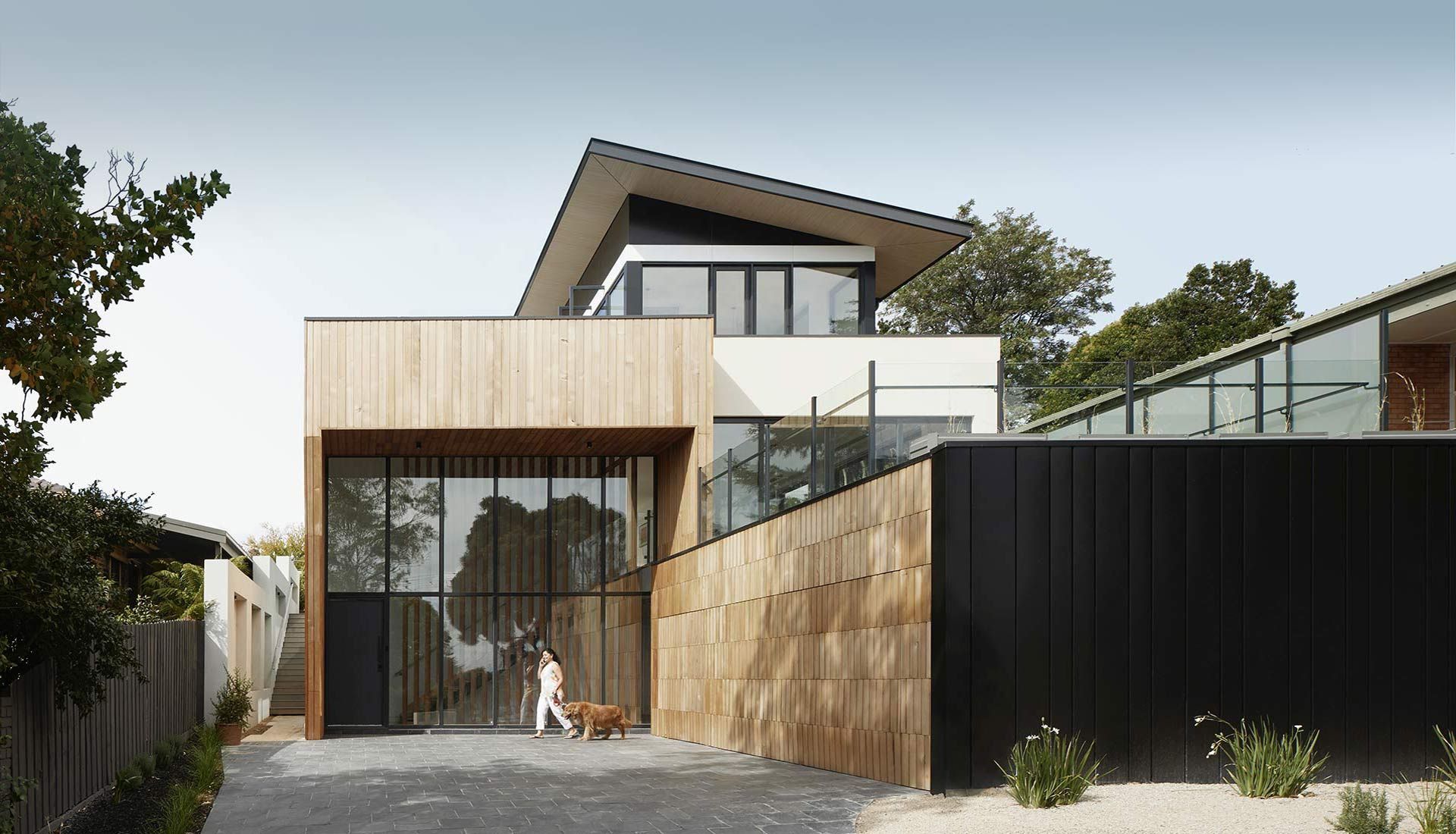 A man walking a dog in front of a modern house.