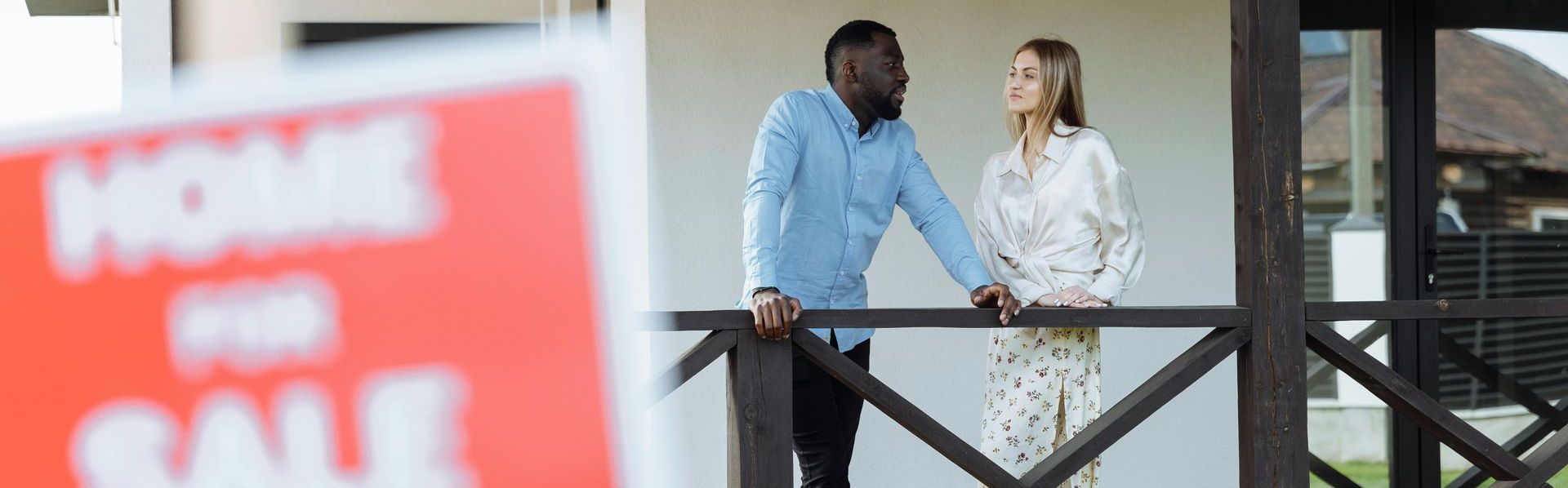 A man and a woman are standing on a porch next to an Orlando area home with a for sale sign.