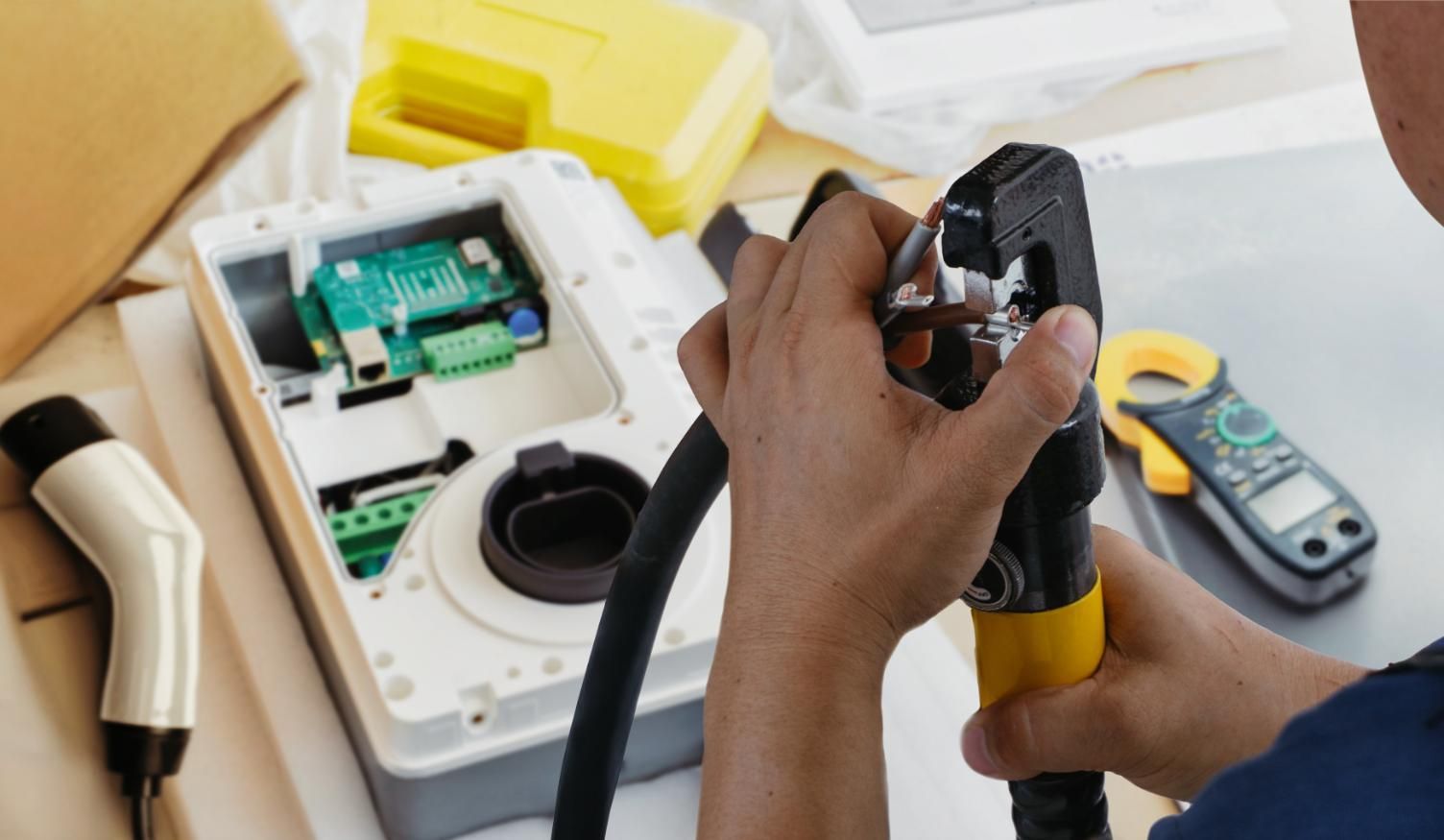 Person working on an EV charger. Holding a crimping tool, open charger components visible.
