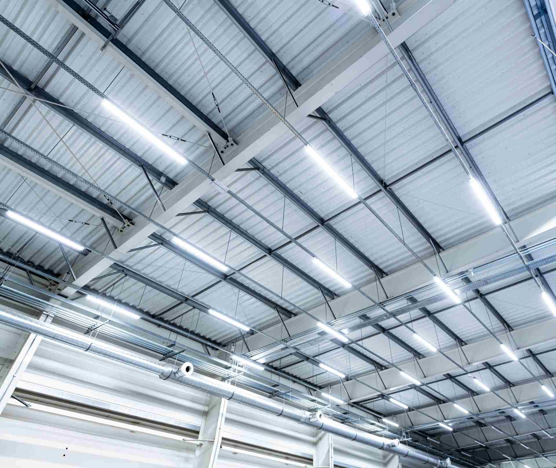 Warehouse ceiling with metal beams, corrugated panels, and fluorescent lights.