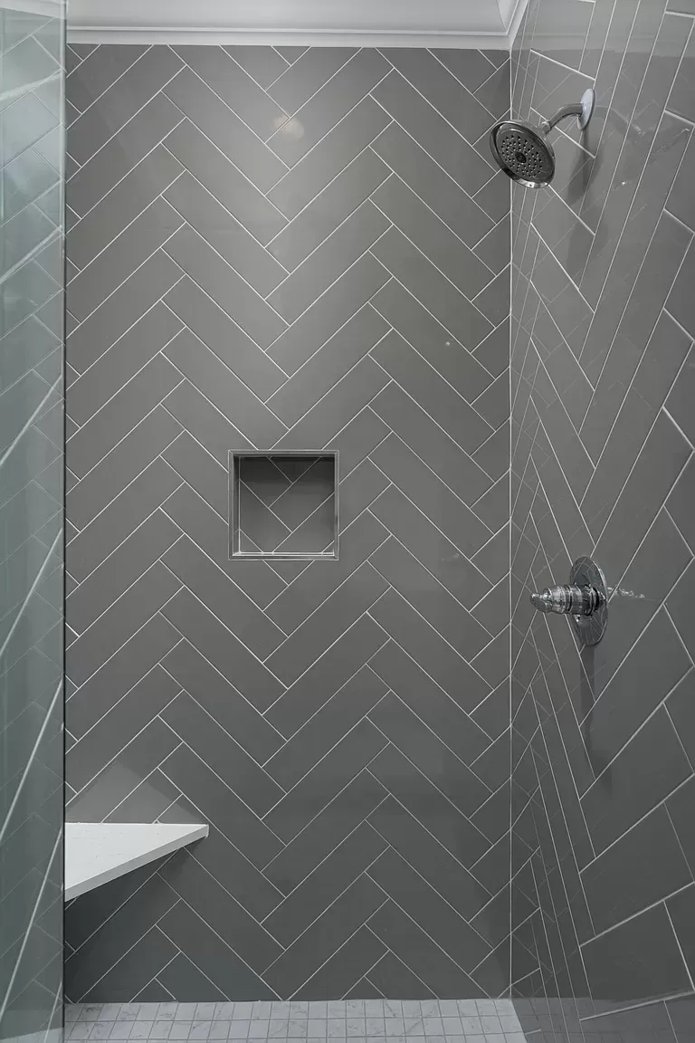 a shower with gray tiles in a herringbone pattern