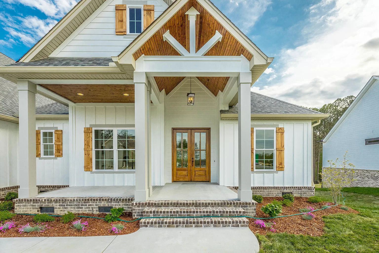 newly built white farm-styled house with brown accents, porch, and double doors.