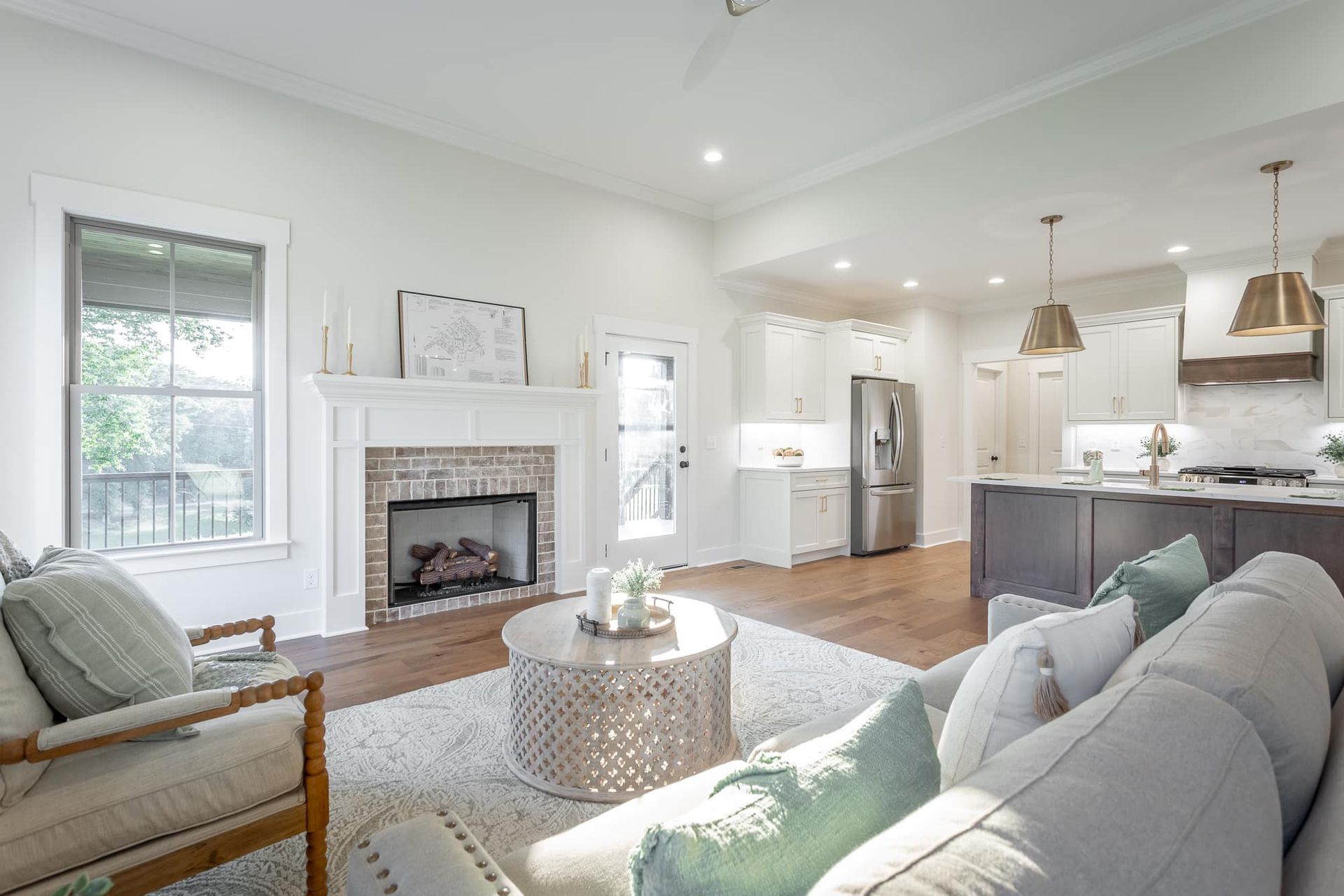 newly designed & constructed Living room with fireplace, open to kitchen; white walls, neutral furniture, hardwood floors, light blue accents.