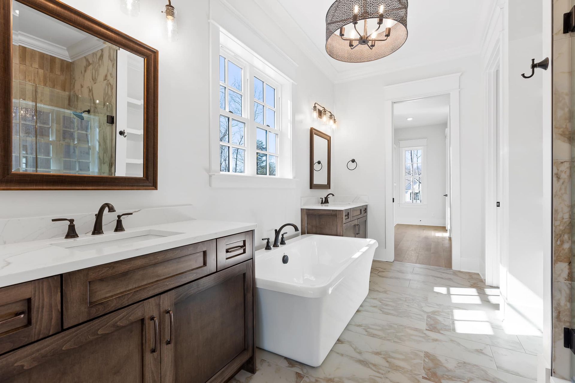 Elegant bathroom with a free-standing tub, white walls, wood cabinets, marble countertops, and large mirror.