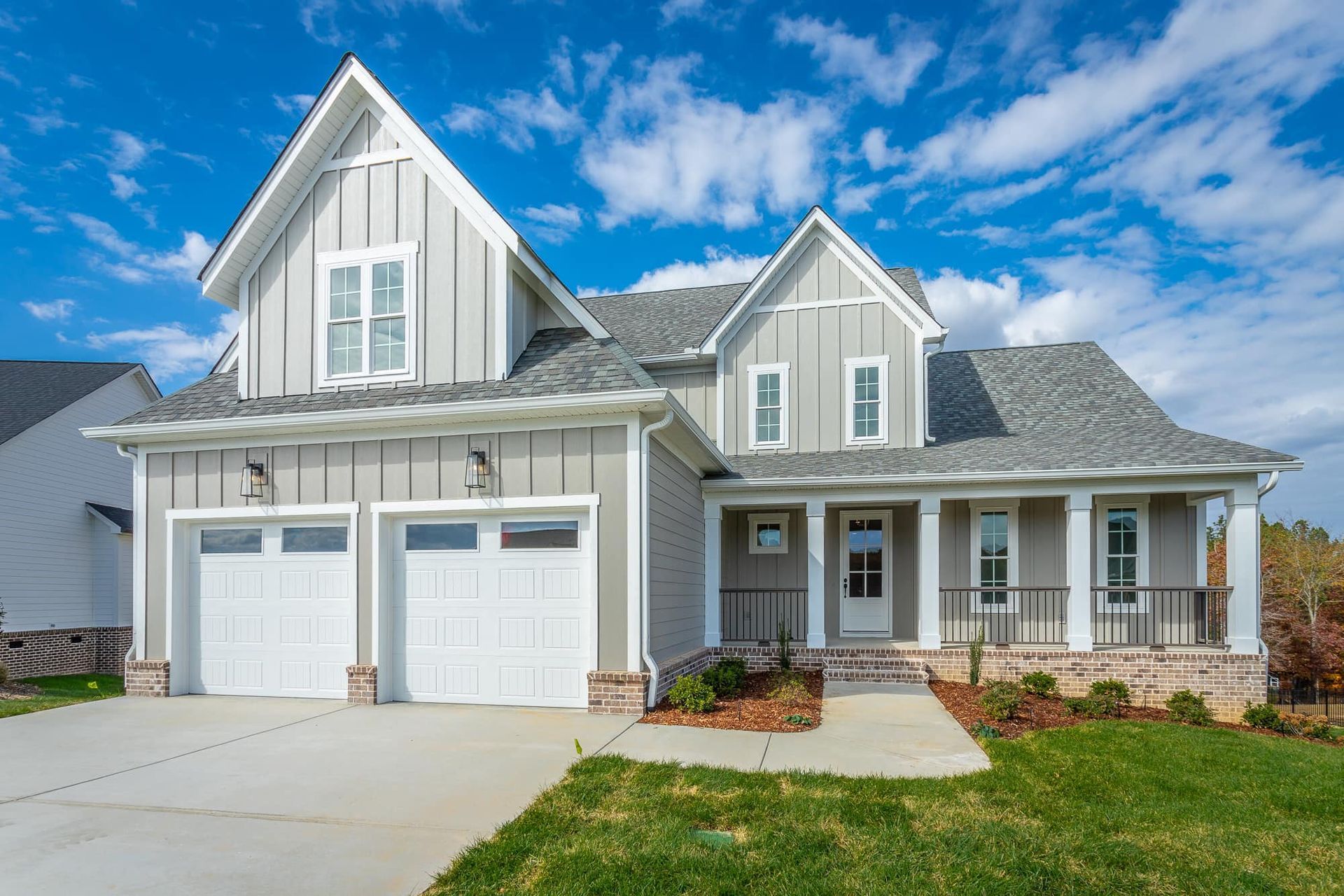 Gray farmhouse with white trim, two-car garage, front porch, and blue sky.