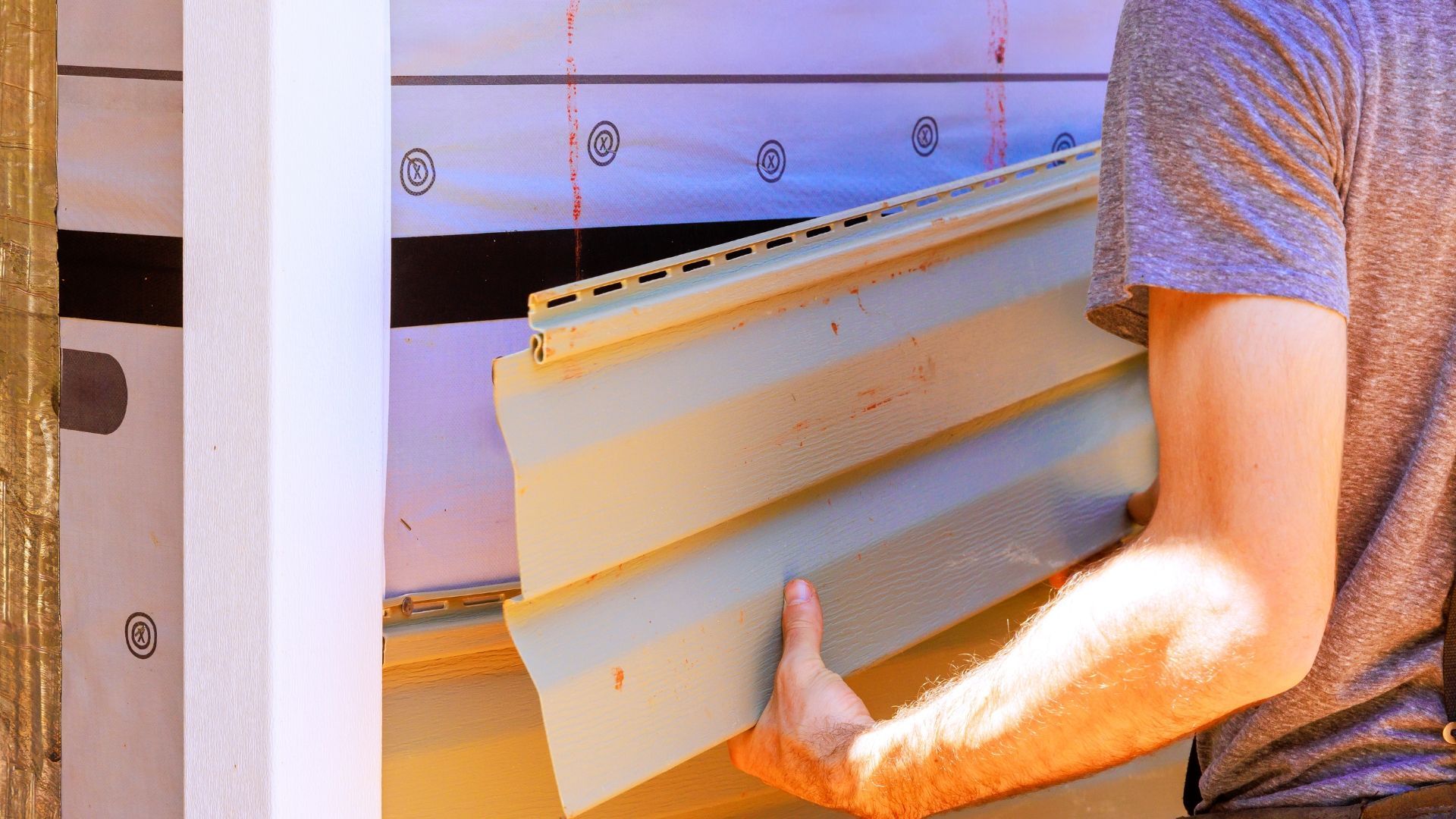 Person holding a stack of white siding panels at a wall installation site