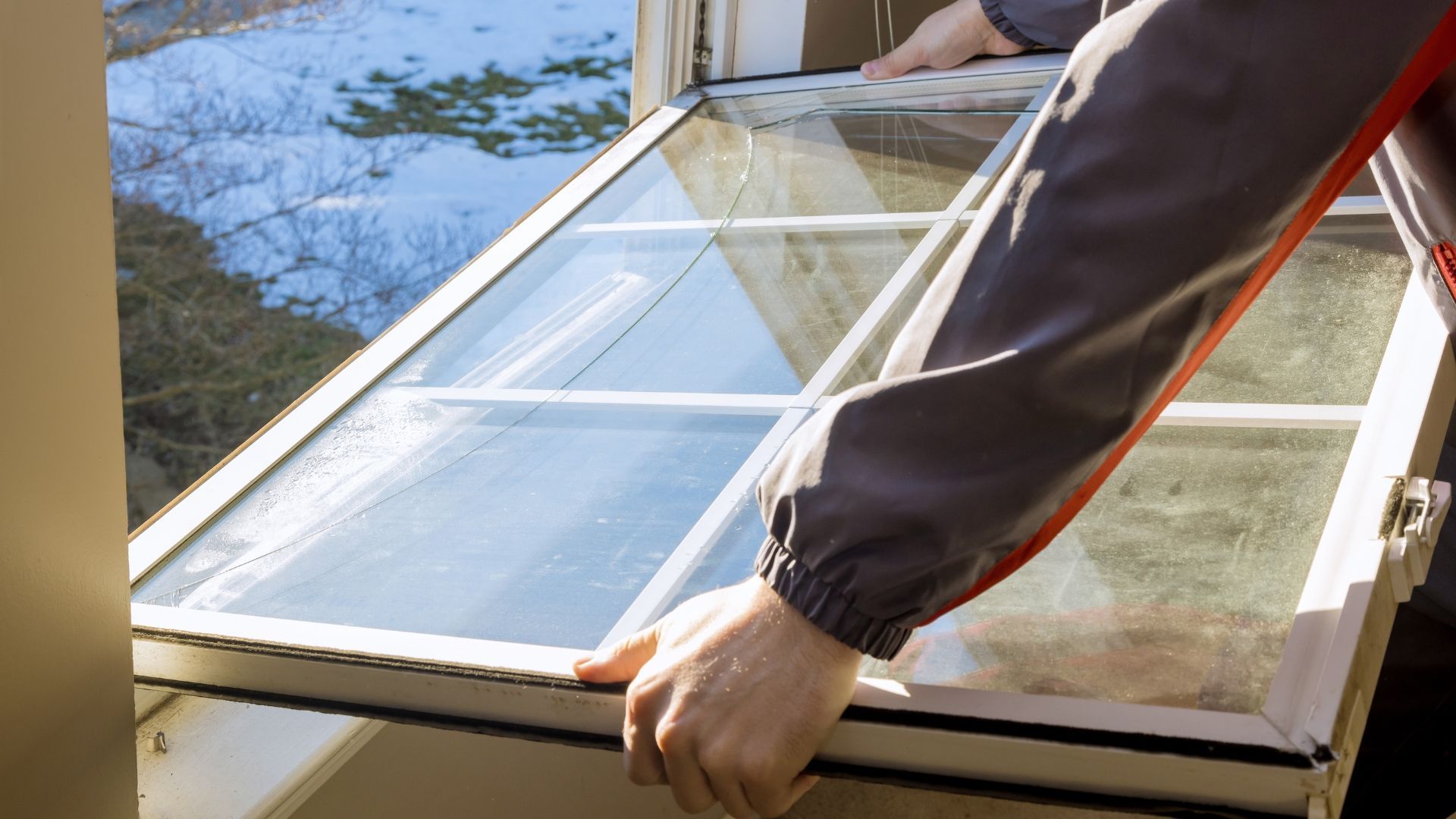 Hands installing a white-framed window outdoors on a sunny day