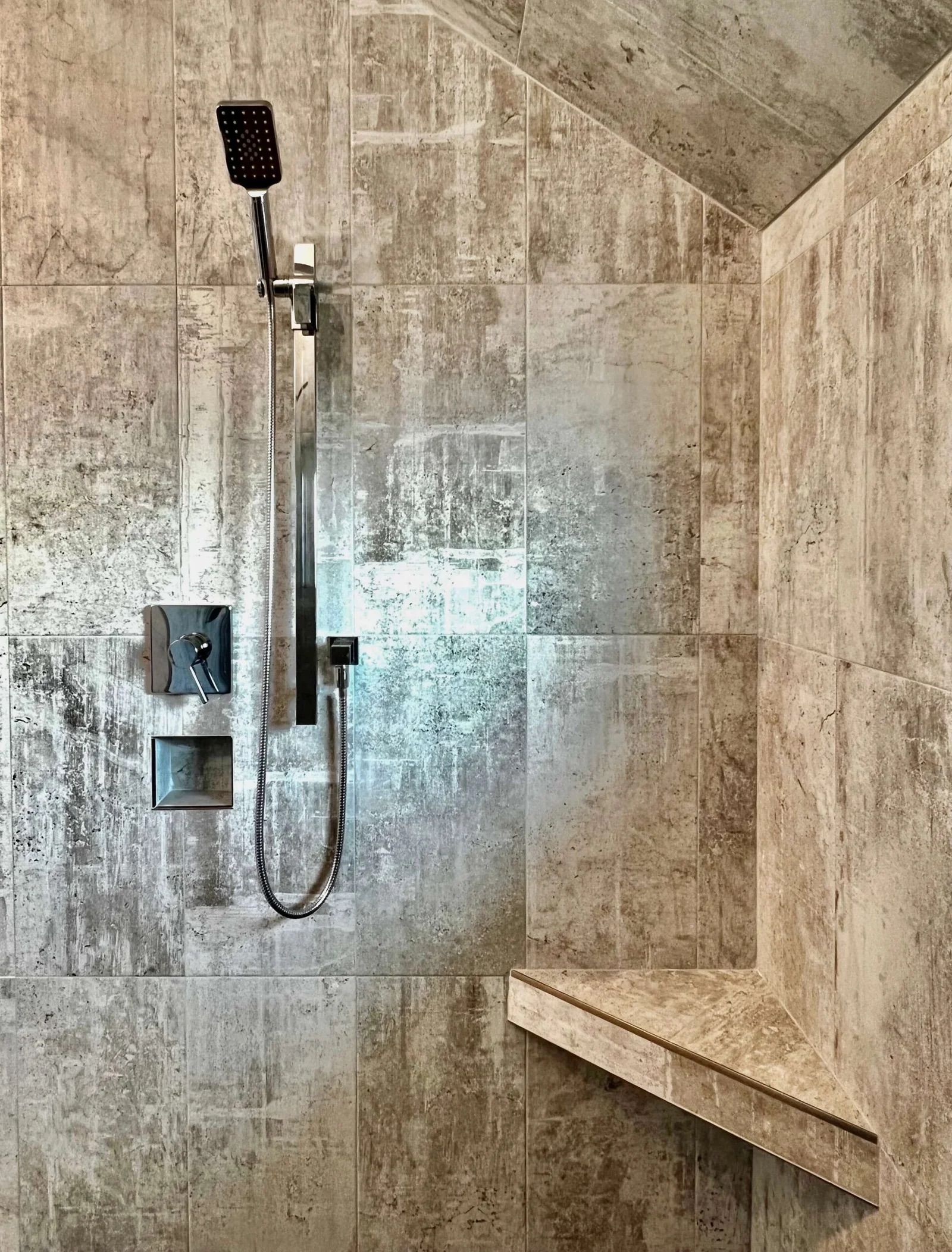 Two workers installing gray wall tiles in a dusty, unfinished room with tools and materials scattered around.