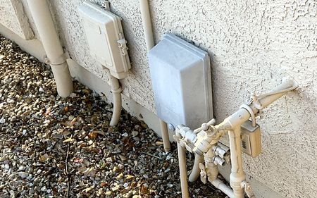 A white box is sitting on the side of a building next to a bunch of pipes.