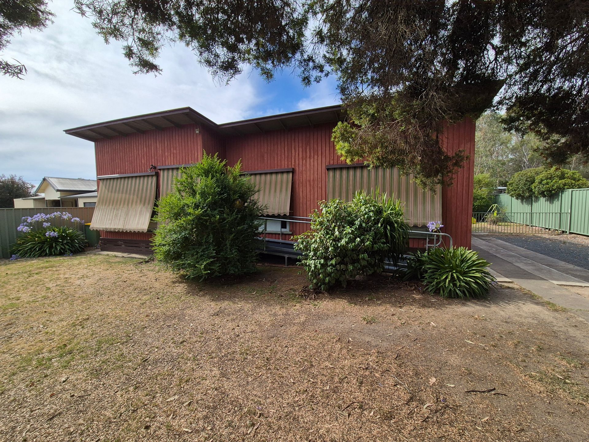 Red building with brown blinds, overgrown bushes, dry grass, and a blue sky. — The Roofer Troopers (NSW) in Howlong, NSW