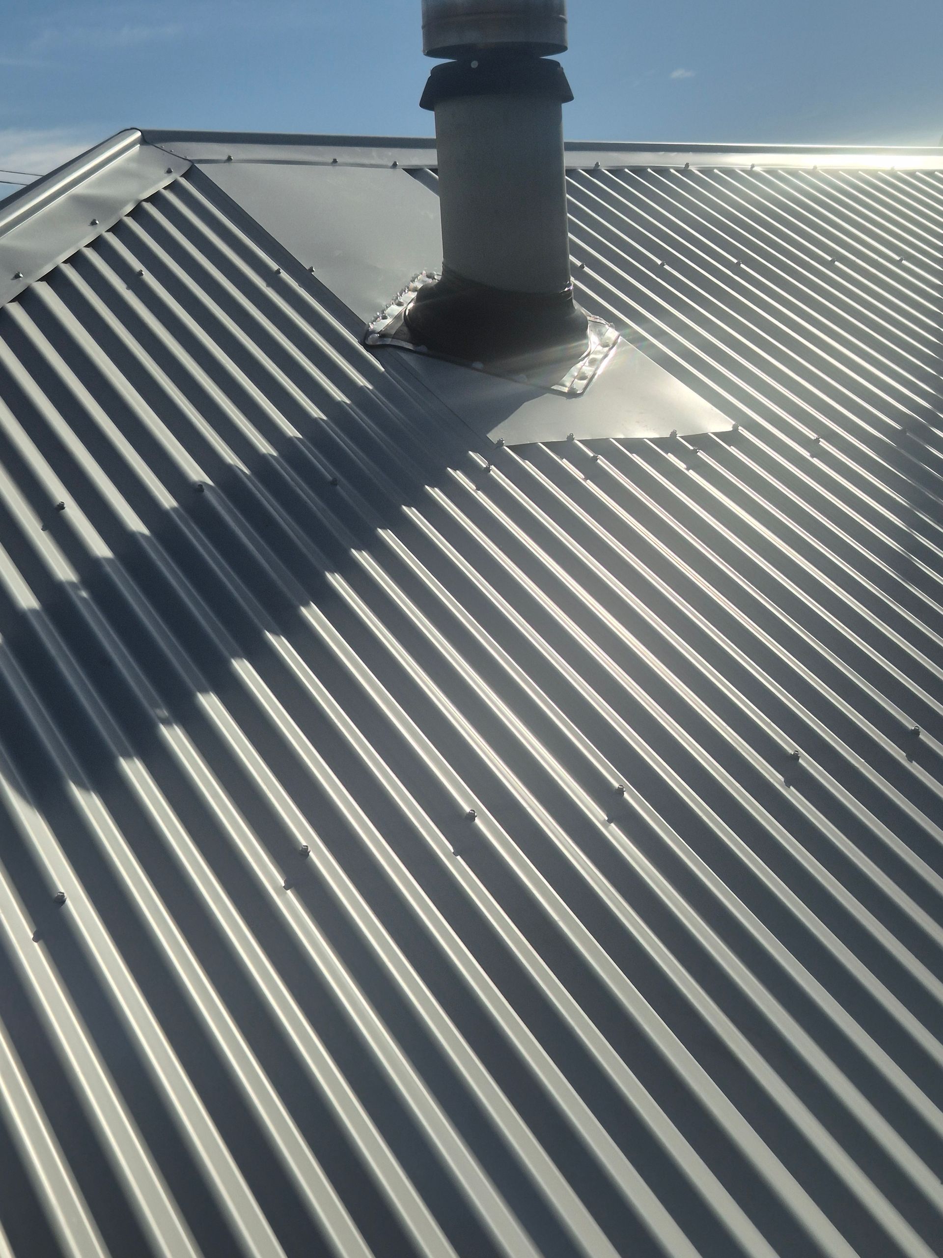 Corrugated metal roof with a chimney, blue sky. — The Roofer Troopers (NSW) in Howlong, NSW