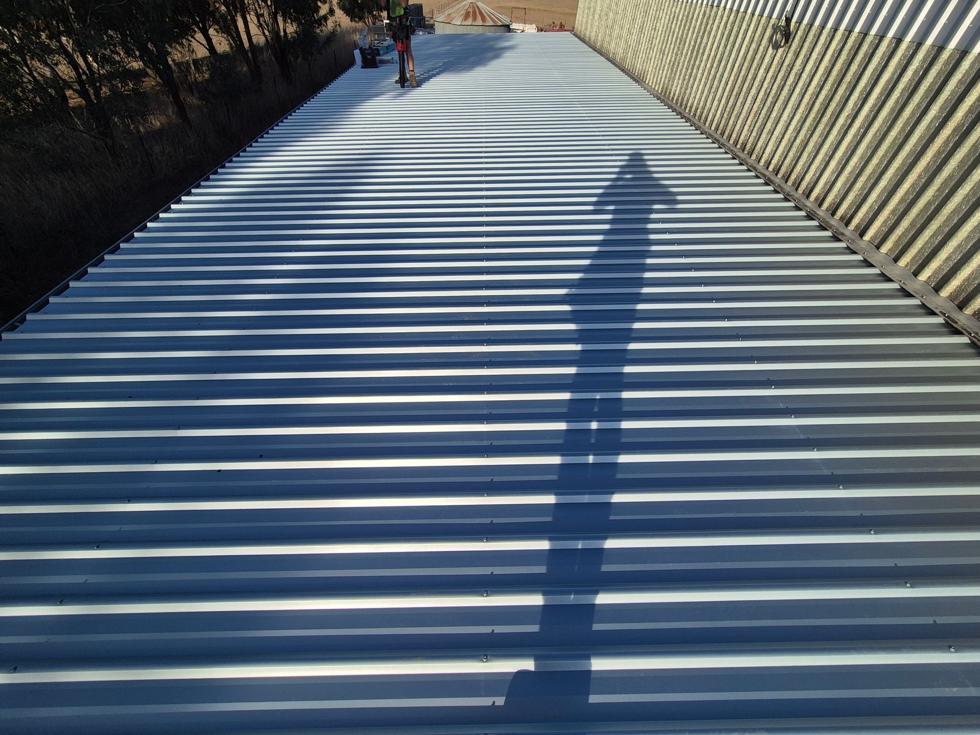 Shadow of a person on a corrugated metal roof, with a person in the distance. — The Roofer Troopers (NSW) in Rutherglen, VIC