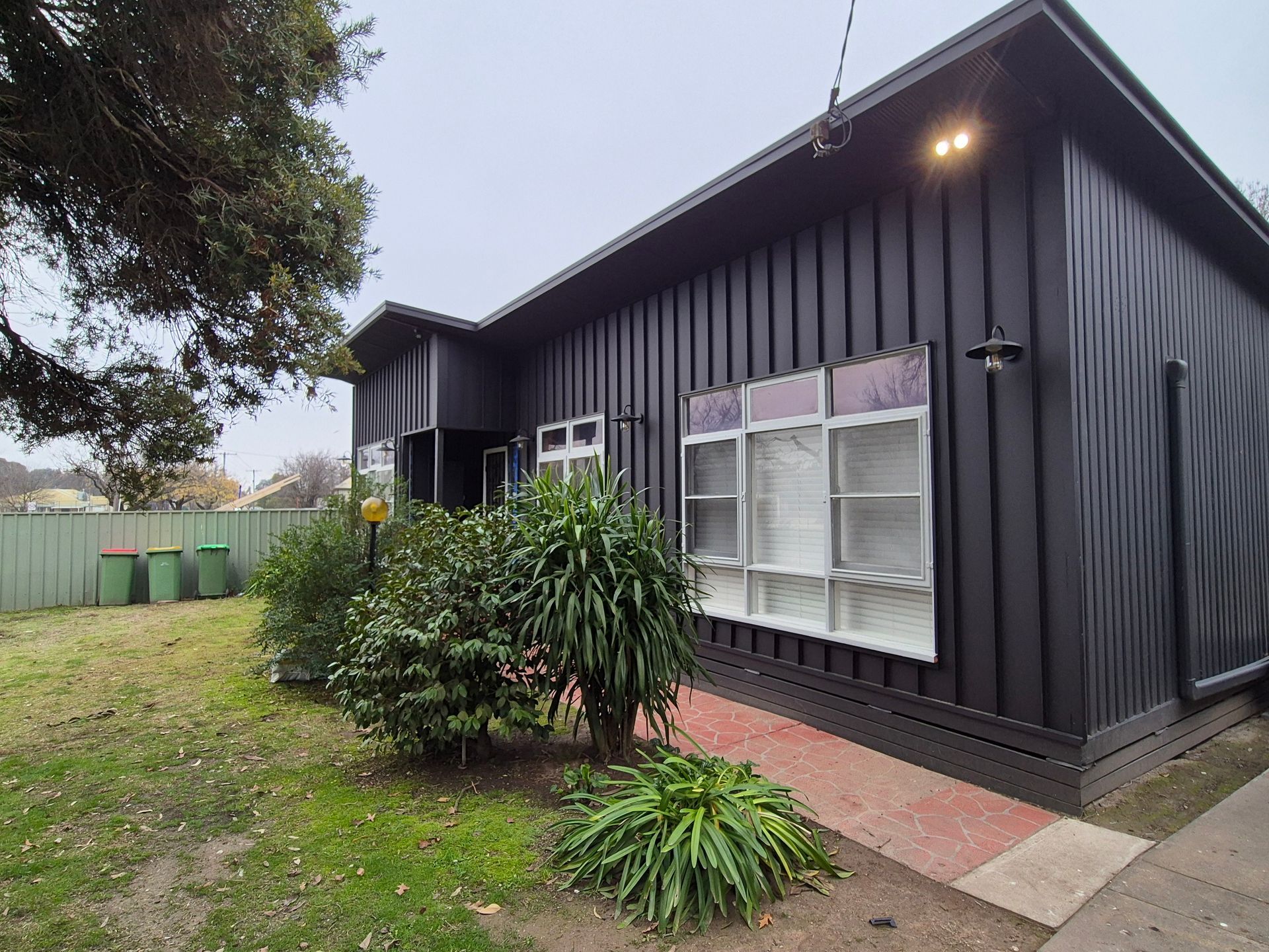 Black house with white-framed windows and red brick path in front, green yard, grey sky. — The Roofer Troopers (NSW) in Rutherglen, VIC
