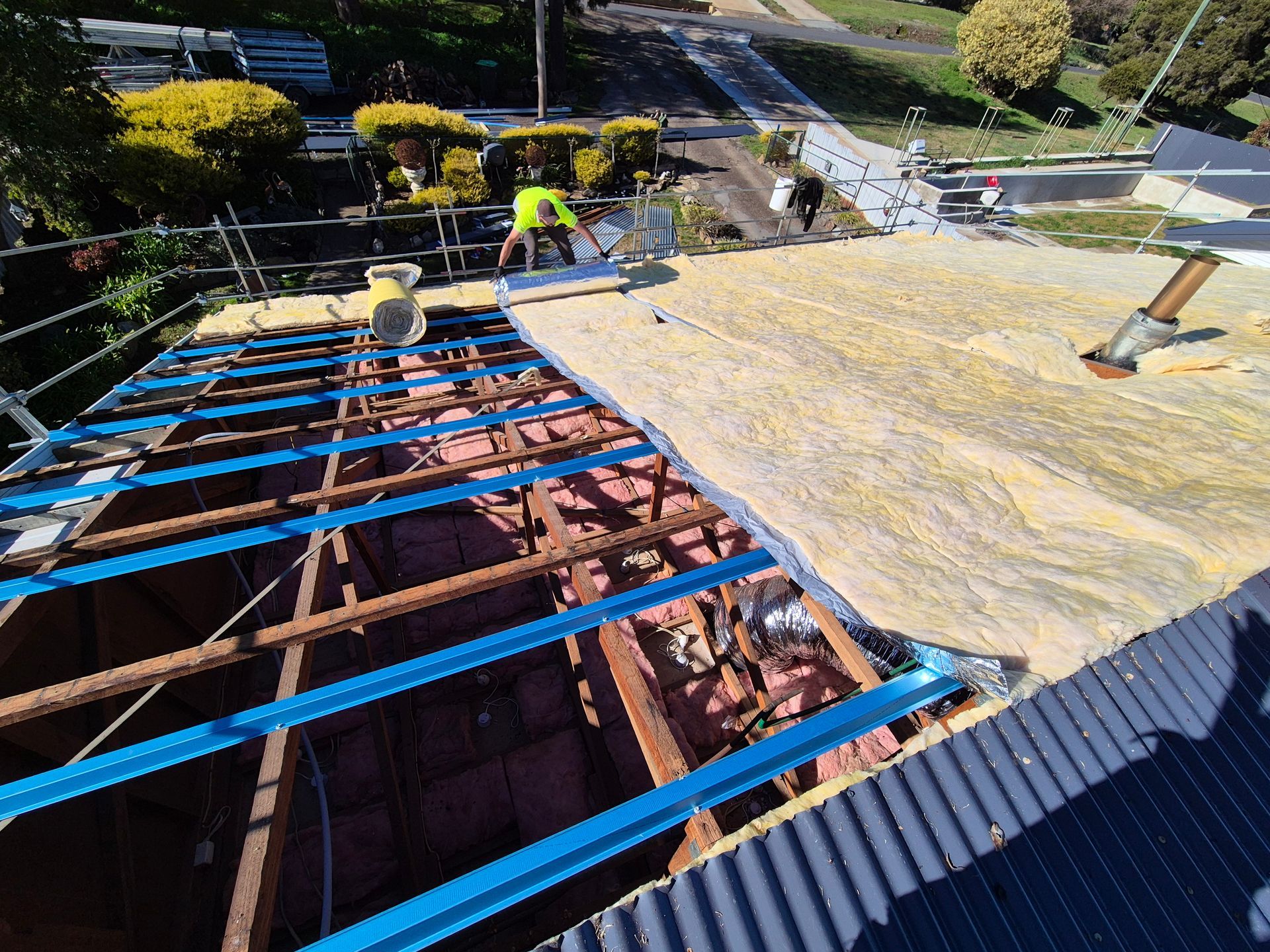 Roof construction: workers installing insulation on an exposed wooden roof frame, with blue metal beams. — The Roofer Troopers (NSW) in Rutherglen, VIC