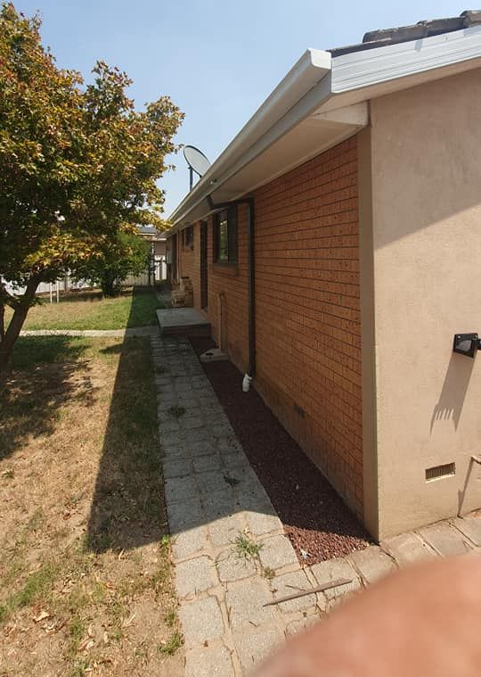 Exterior view of a brick building with a pathway, gutter, and greenery on a sunny day. — The Roofer Troopers (NSW) in Rutherglen, VIC