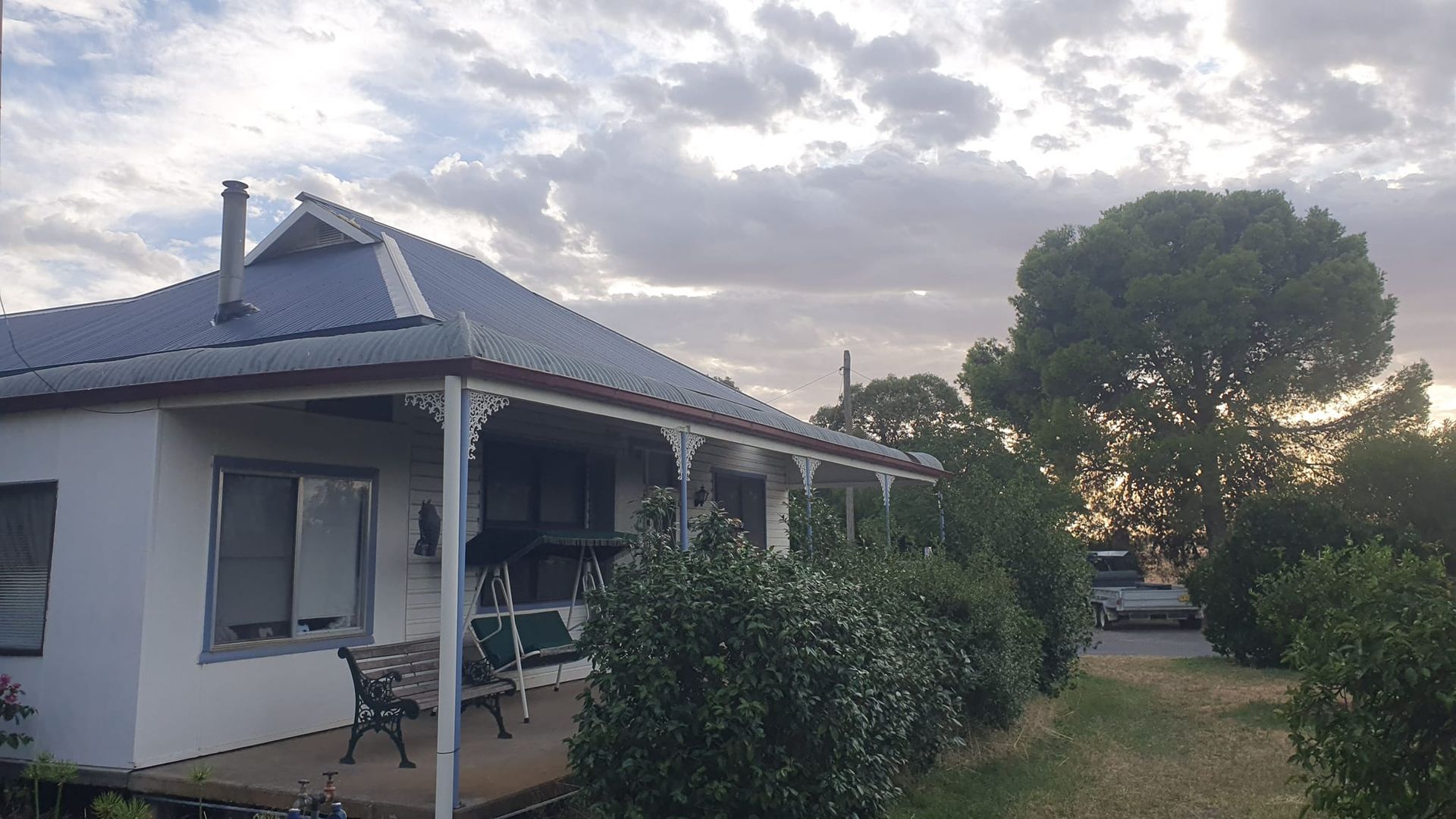 White house with a porch and shrubs, set against a cloudy sky. — The Roofer Troopers (NSW) in Rutherglen, VIC