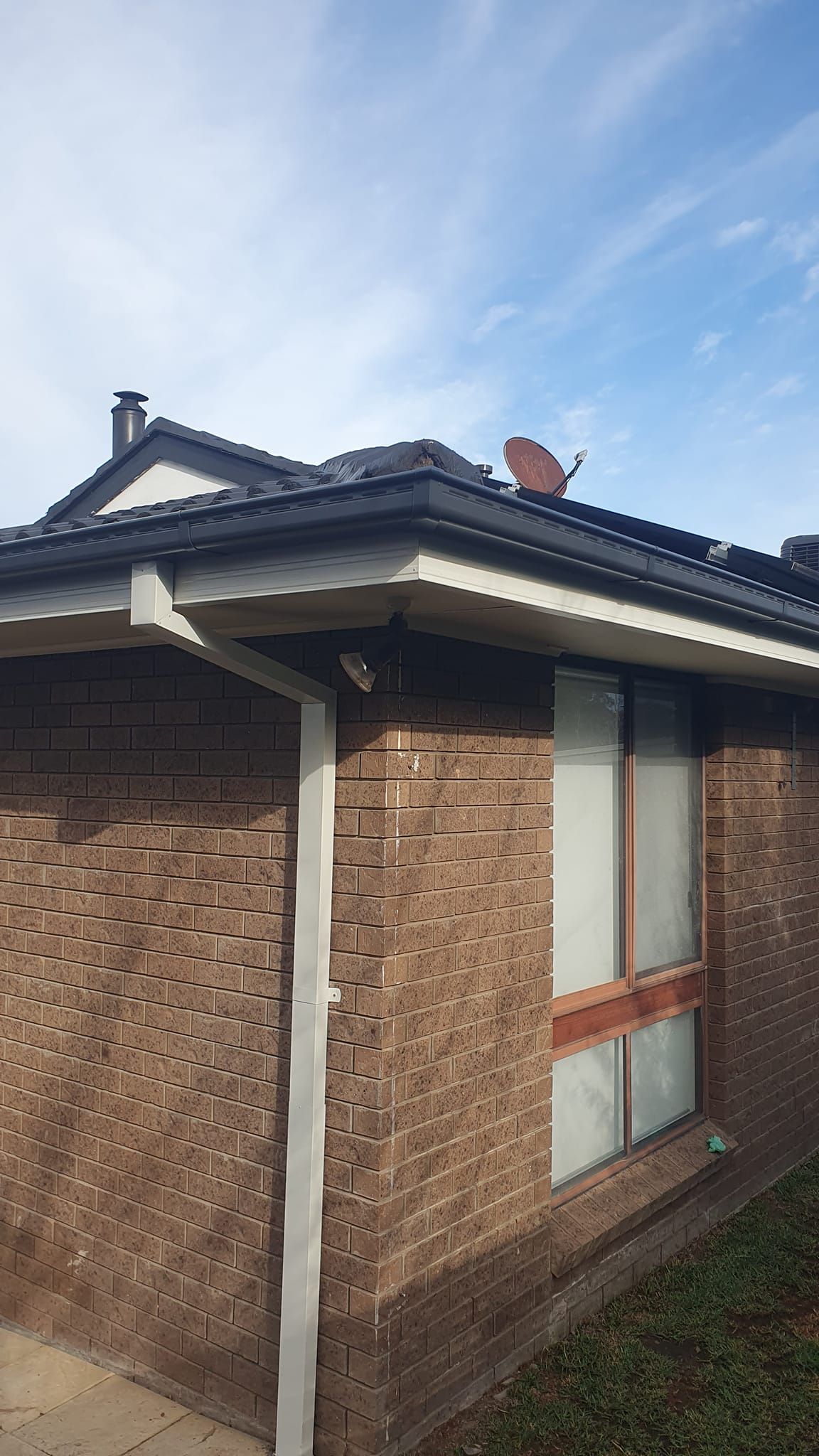 Brick house corner with gray roof, satellite dish, and window under a cloudy sky. — The Roofer Troopers (NSW) in Rutherglen, VIC