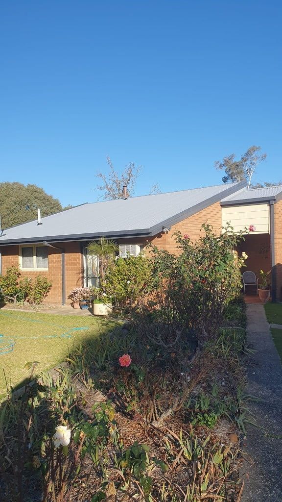 Brick Building With Gray Roof and Overgrown Bushes in Front — The Roofer Troopers (NSW) in Howlong, NSW