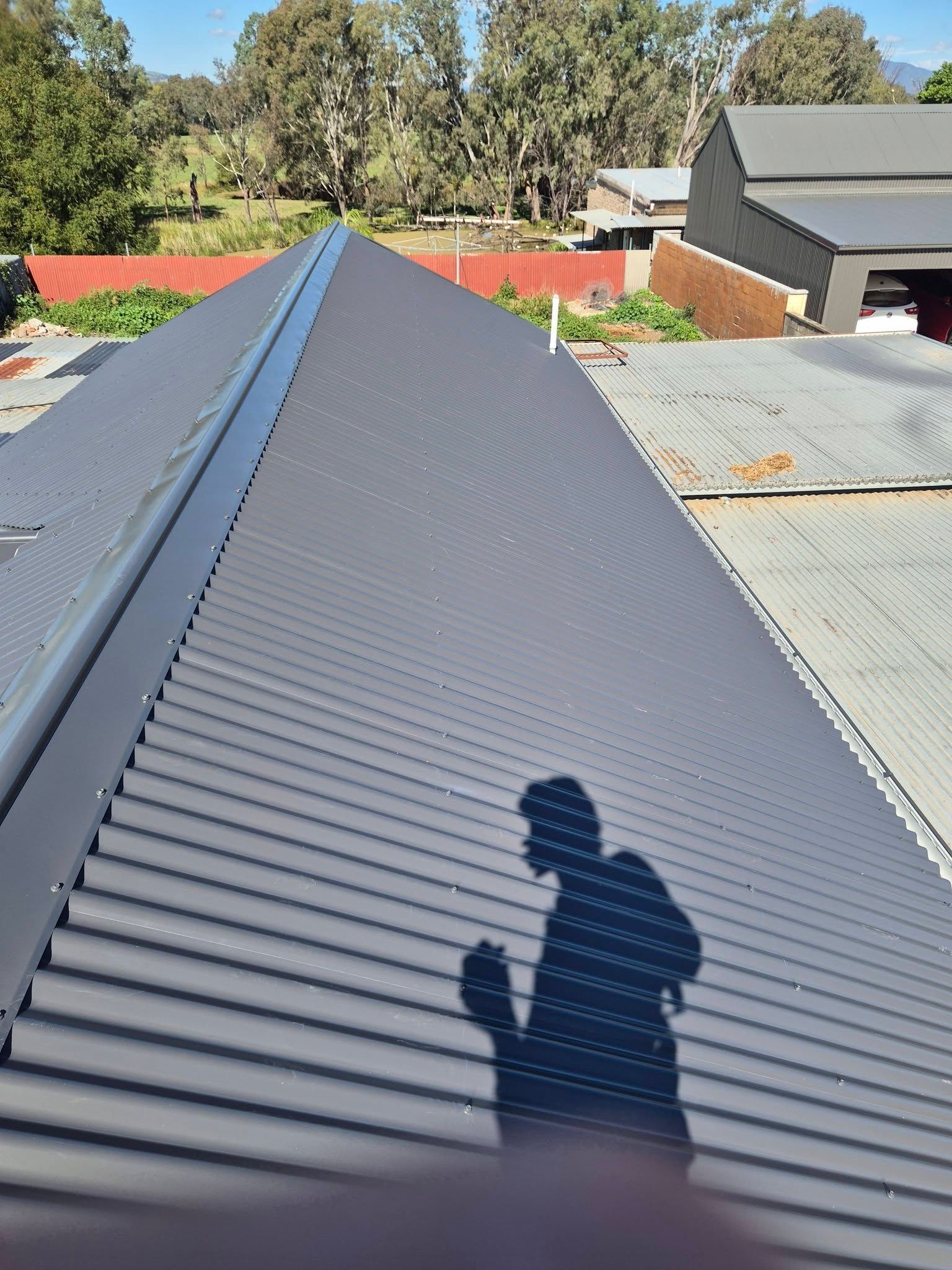 Person’s Shadow on a Gray Metal Roof Beside Neighboring Houses and Trees — The Roofer Troopers in Wodonga, VIC