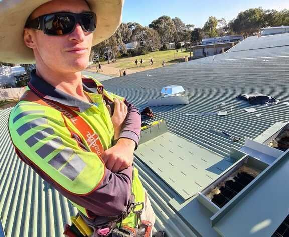 Man In Safety Gear On A Metal Roof, Arms Crossed, Wearing Sunglasses — The Roofer Troopers (NSW) in Howlong, NSW