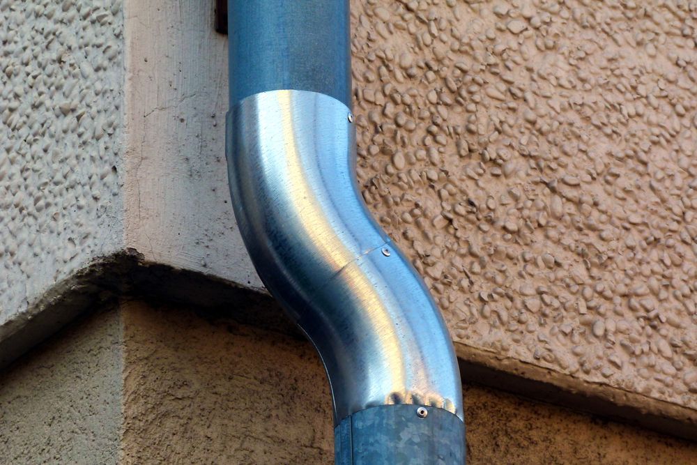 Curved Silver Downspout Attached to a Building Corner — The Roofer Troopers in Wodonga, VIC