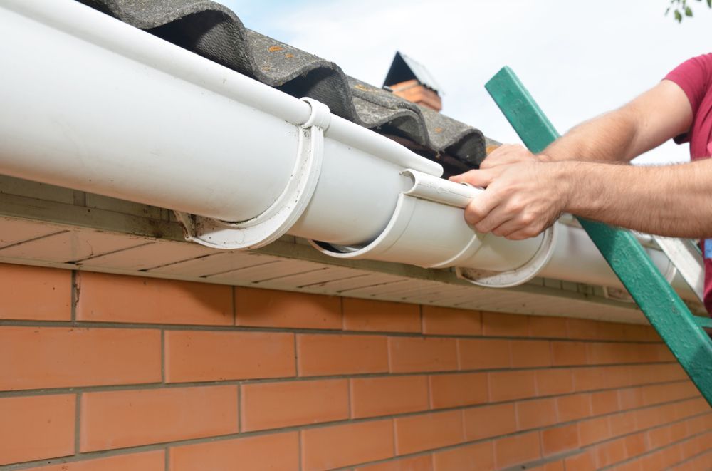 Hands Installing a White Gutter on a Brick Wall Using a Green Level — The Roofer Troopers in Wodonga, VIC