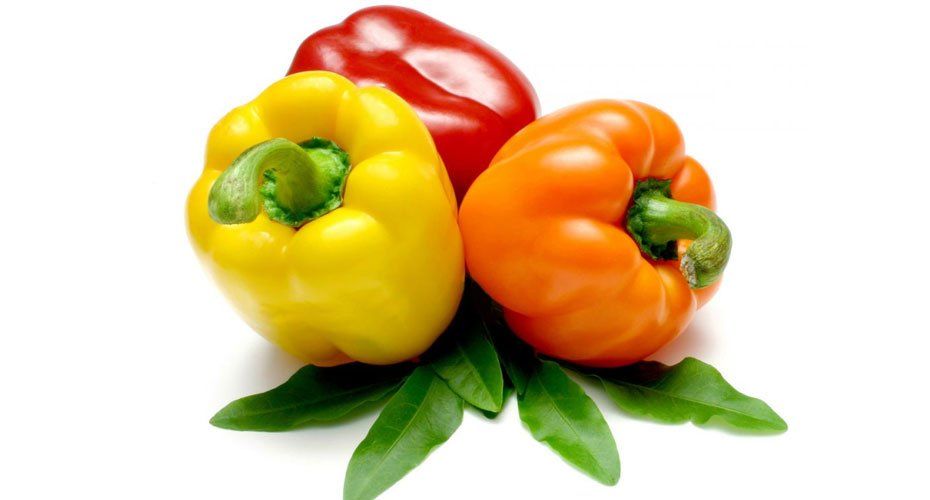 Three different colored peppers with green leaves on a white background