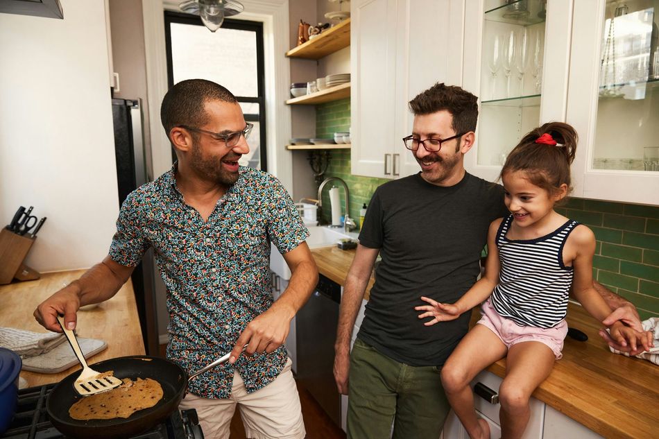 Two men and a little girl are cooking together in a kitchen.