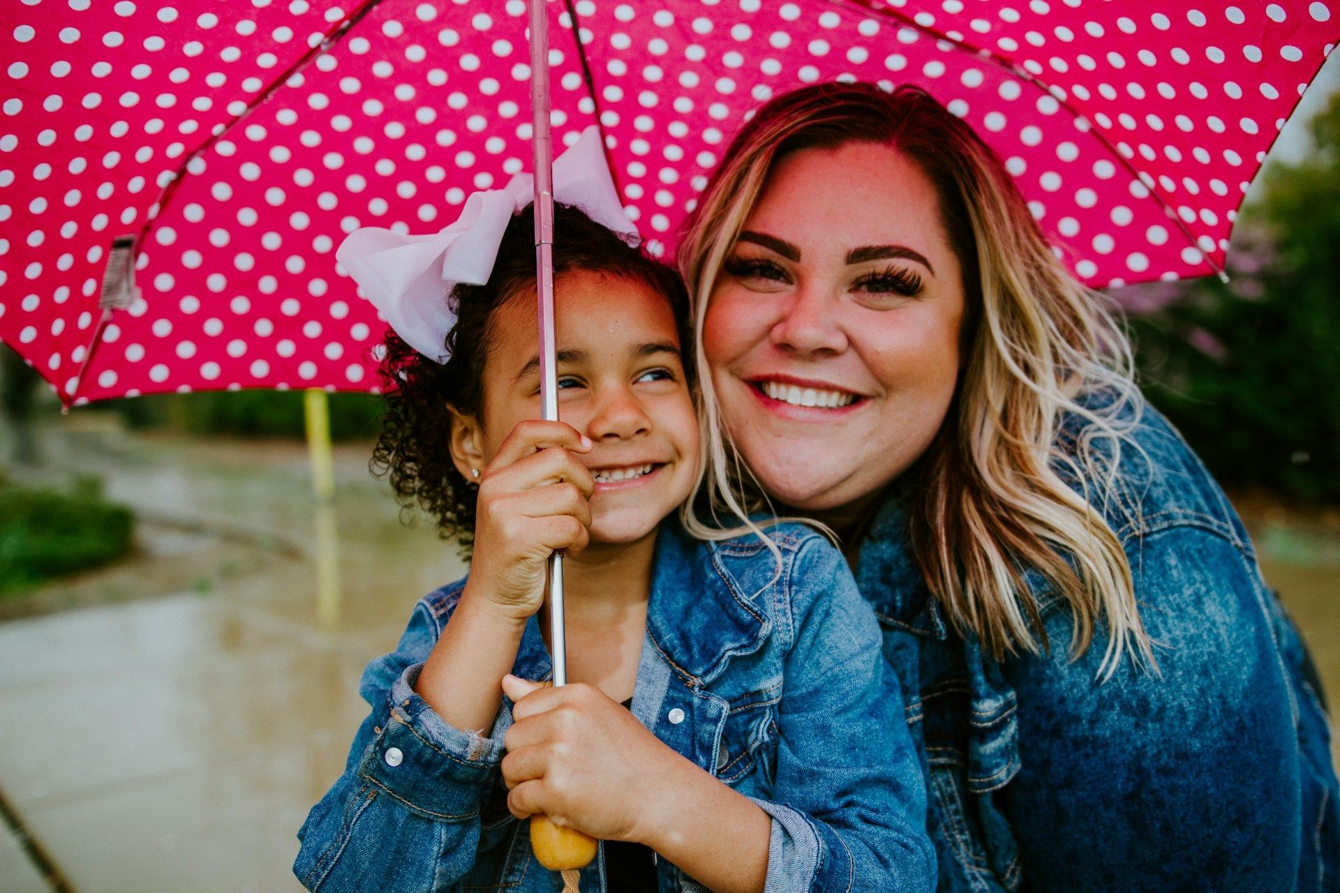 Smiling woman and child under a pink polka-dot umbrella outdoors