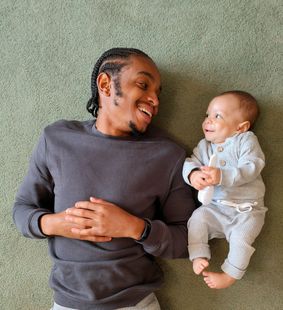 A man is laying on the floor with a baby.