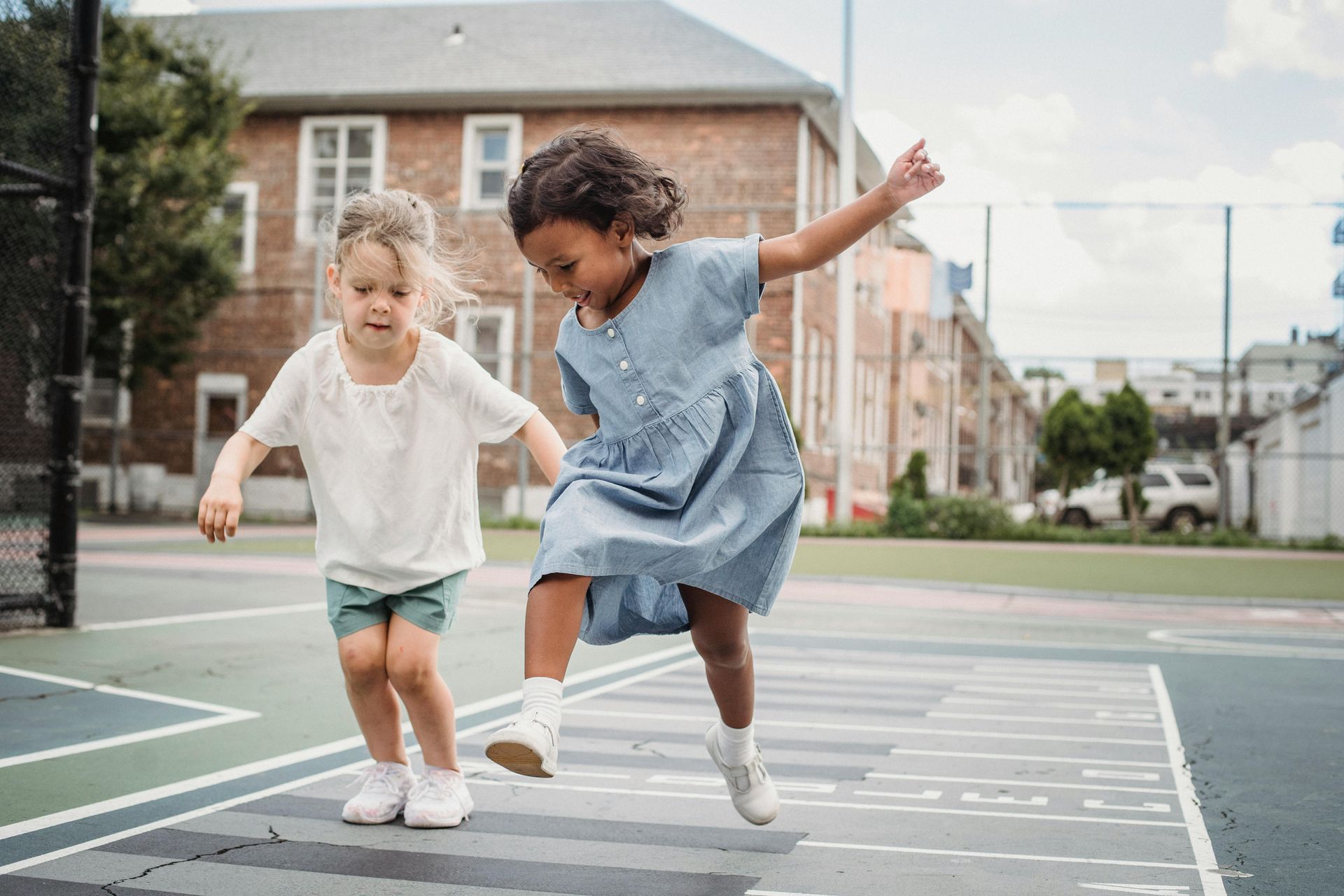 Two little girls are playing hopscotch on a court.