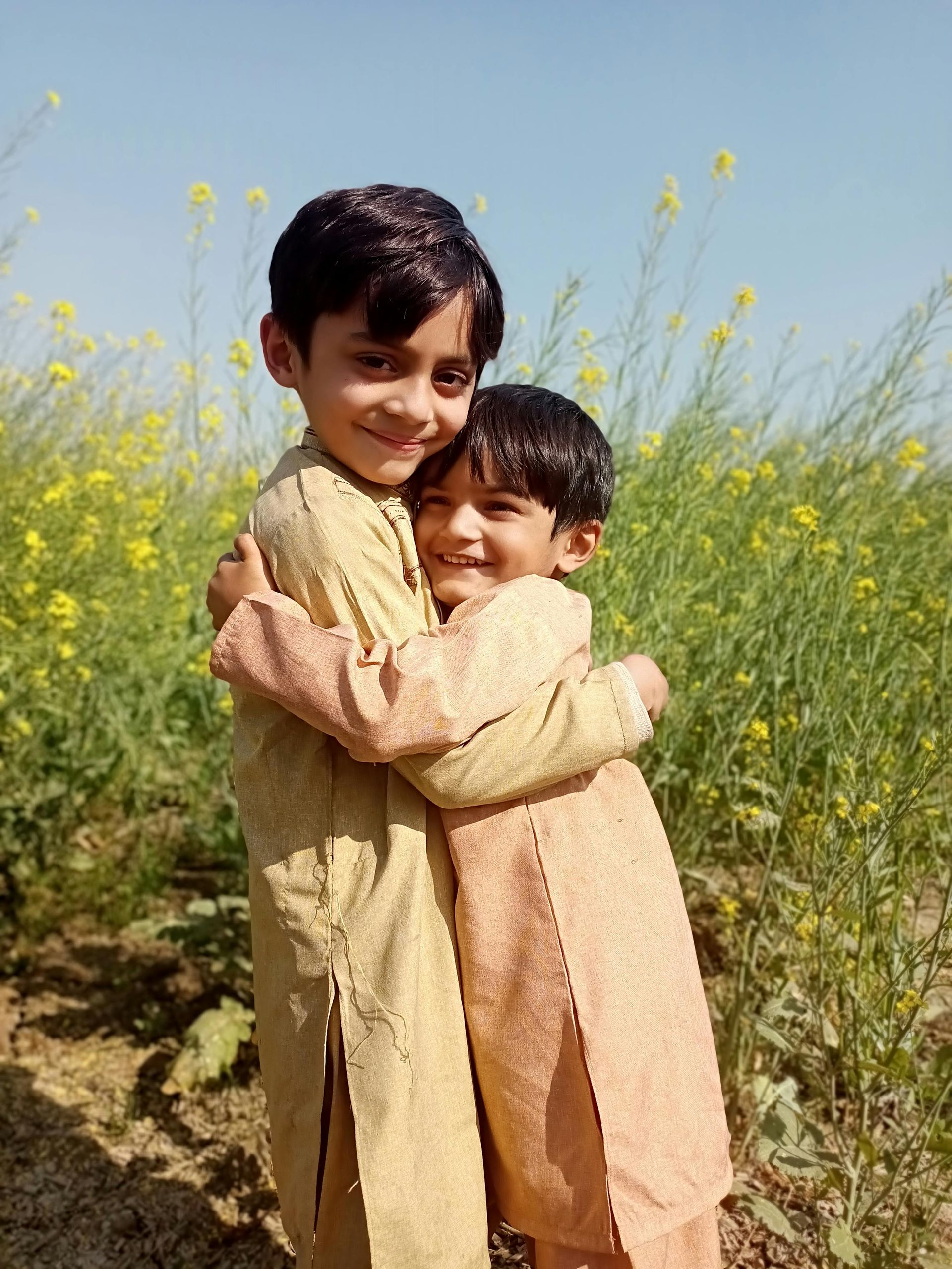 Two young boys are hugging each other in a field of yellow flowers.