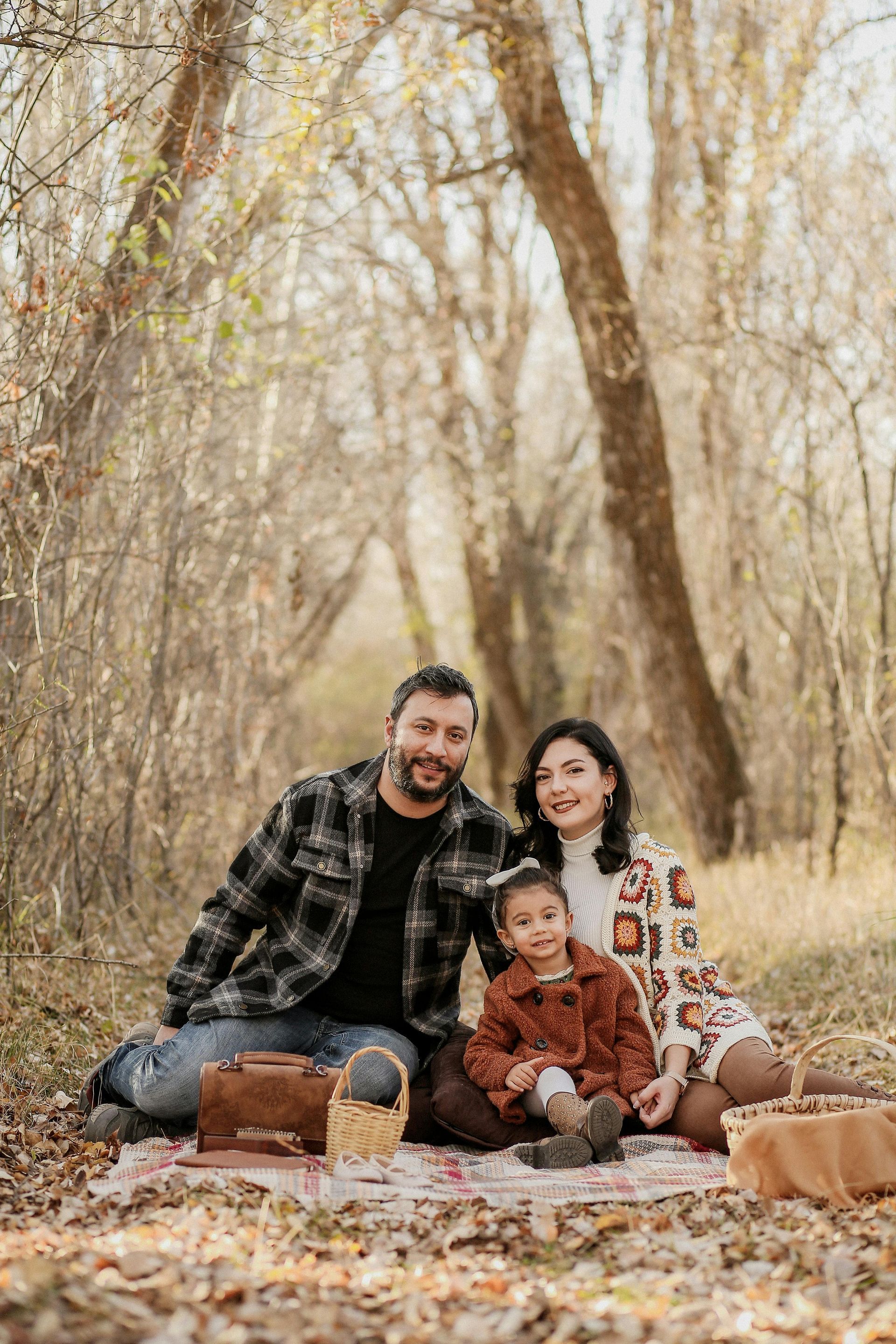 A family is sitting on a blanket in the woods.