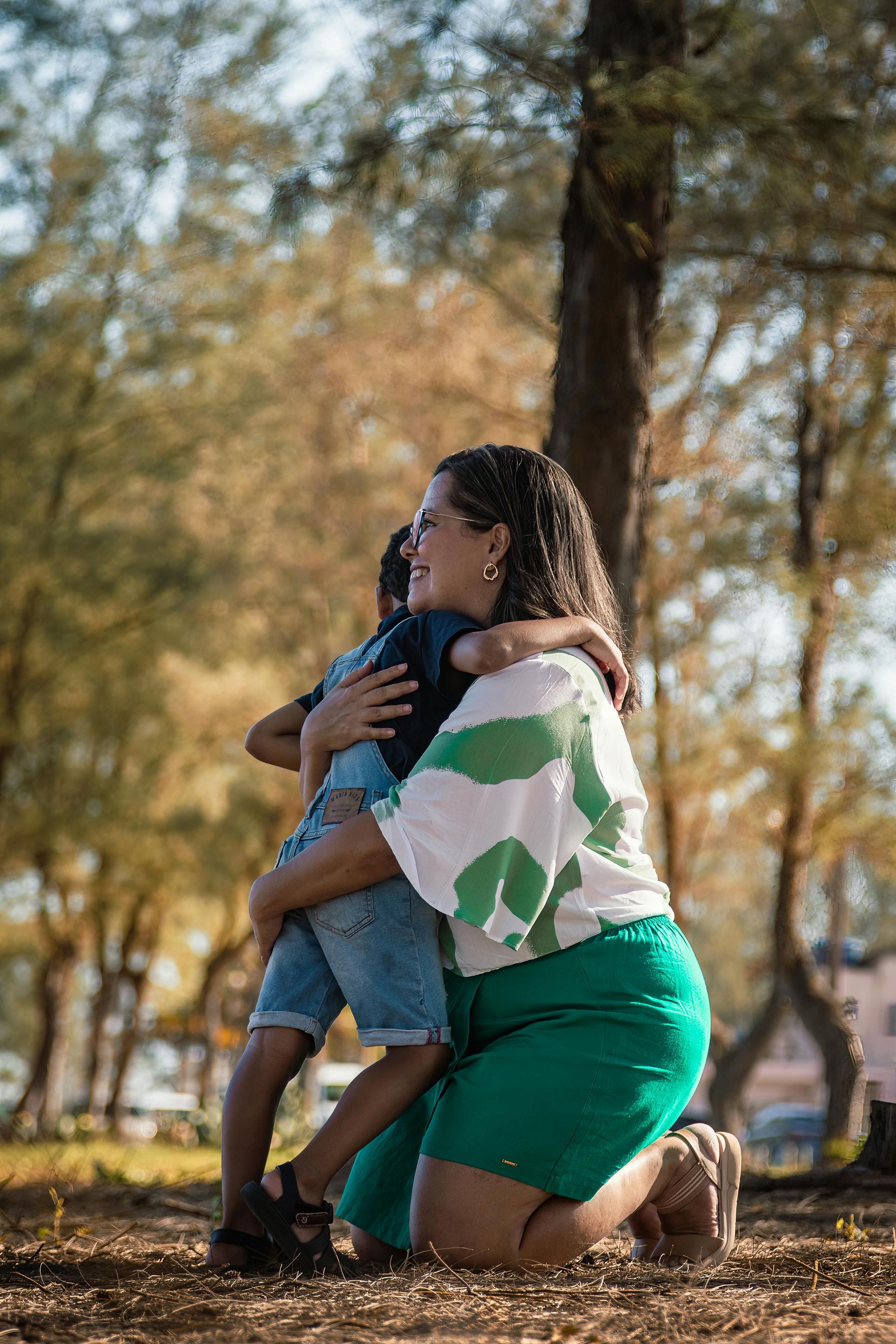 A woman is kneeling down and hugging a child in a park.