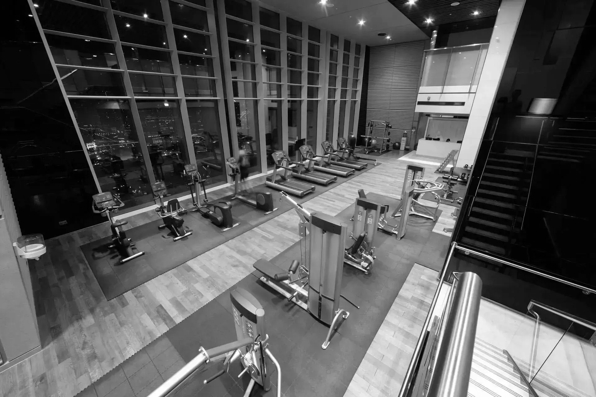 A black and white photo of a gym with treadmills and stairs.