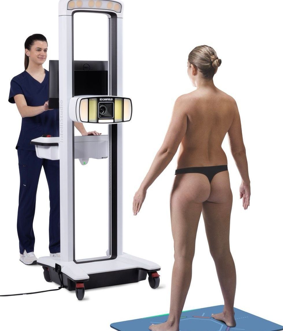 Eine Frau im Stringtanga steht vor einem Körperscanner; eine Krankenschwester bedient die Steuerung. Weißer Hintergrund.