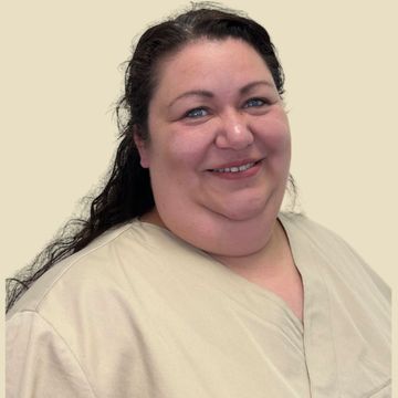 Frau in beigefarbener Kasack, lächelnd, in einem runden Rahmen vor neutralem Hintergrund.