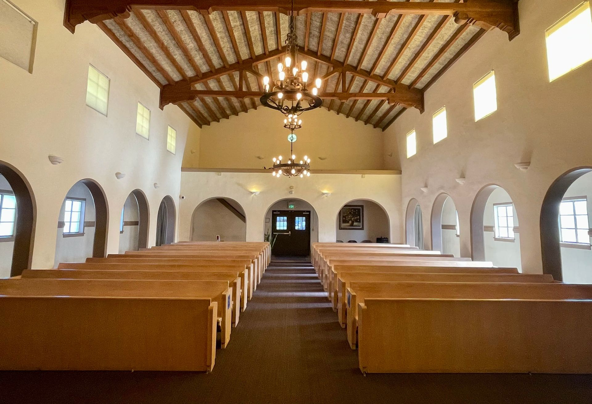 Two people in black suits carry a wooden casket with white flower arrangement.