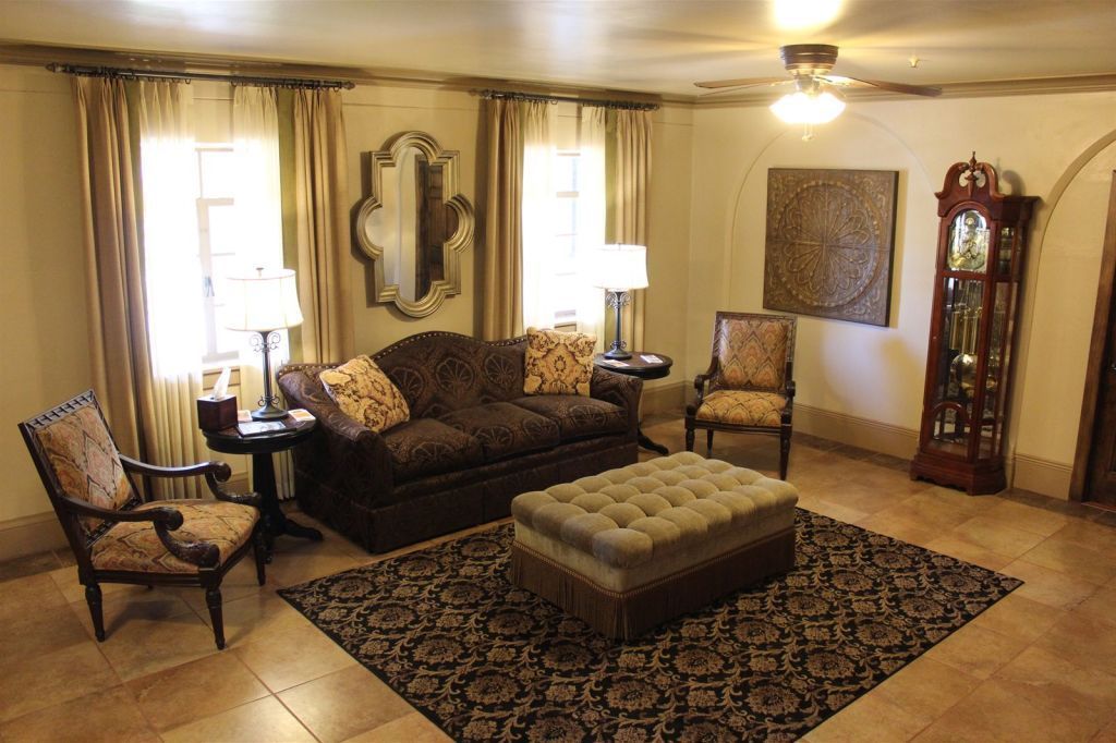 Living room with sofa, chairs, rug, and mirror; beige walls, brown furniture, and tile floor.