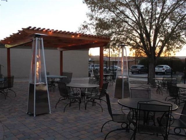 Outdoor patio with tables, chairs, and two pyramid patio heaters under a wooden pergola.