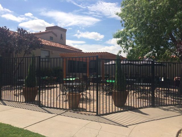 Black metal fence encloses outdoor patio with tables, chairs, potted plants, and building in the background.