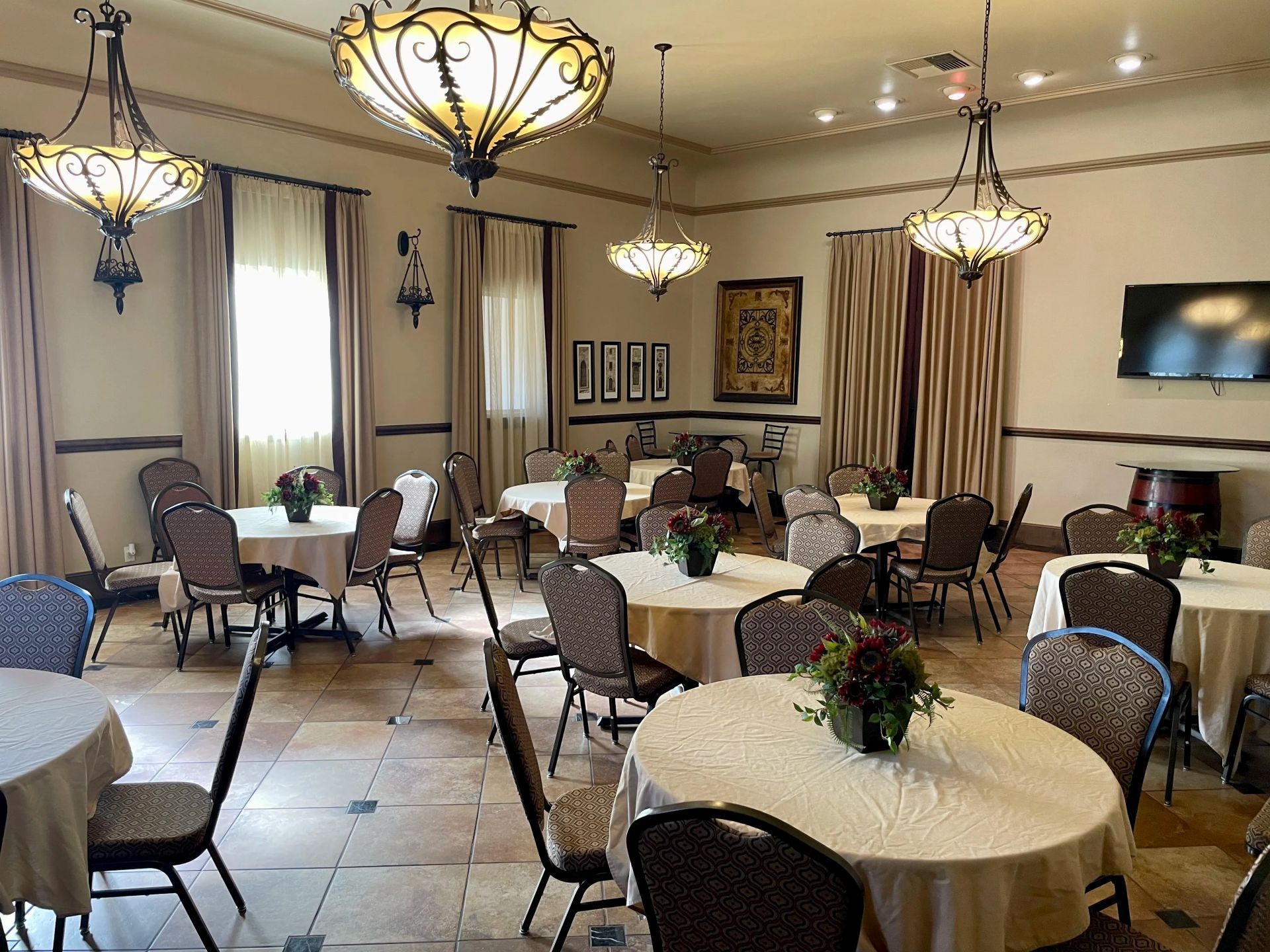Elegant dining room with round tables, chairs, chandeliers, and floral centerpieces.