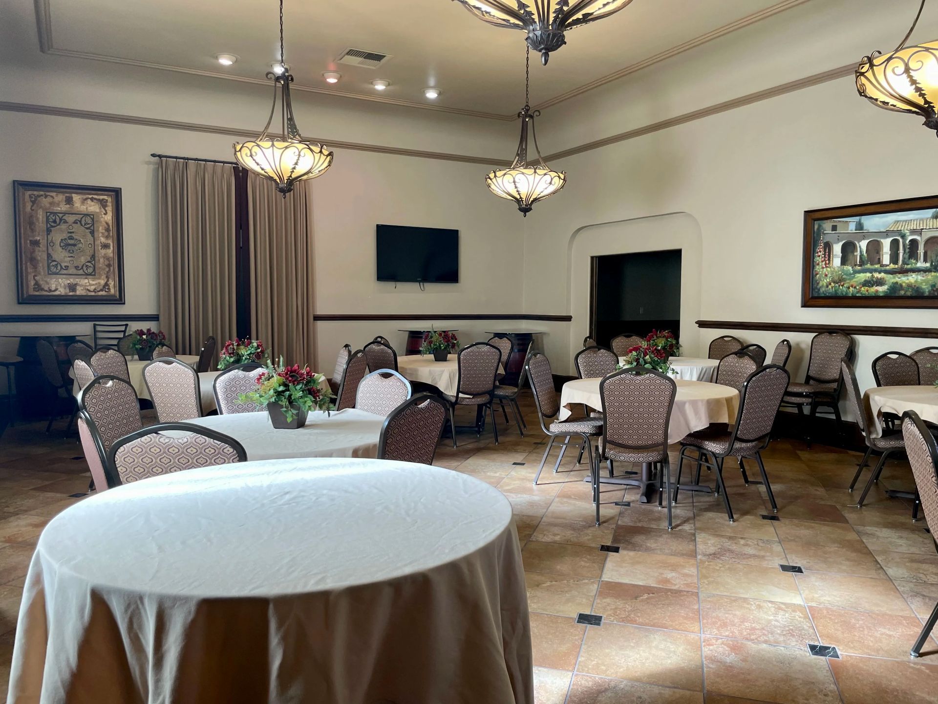 Banquet hall with round tables set for a meal; beige tablecloths, floral centerpieces.
