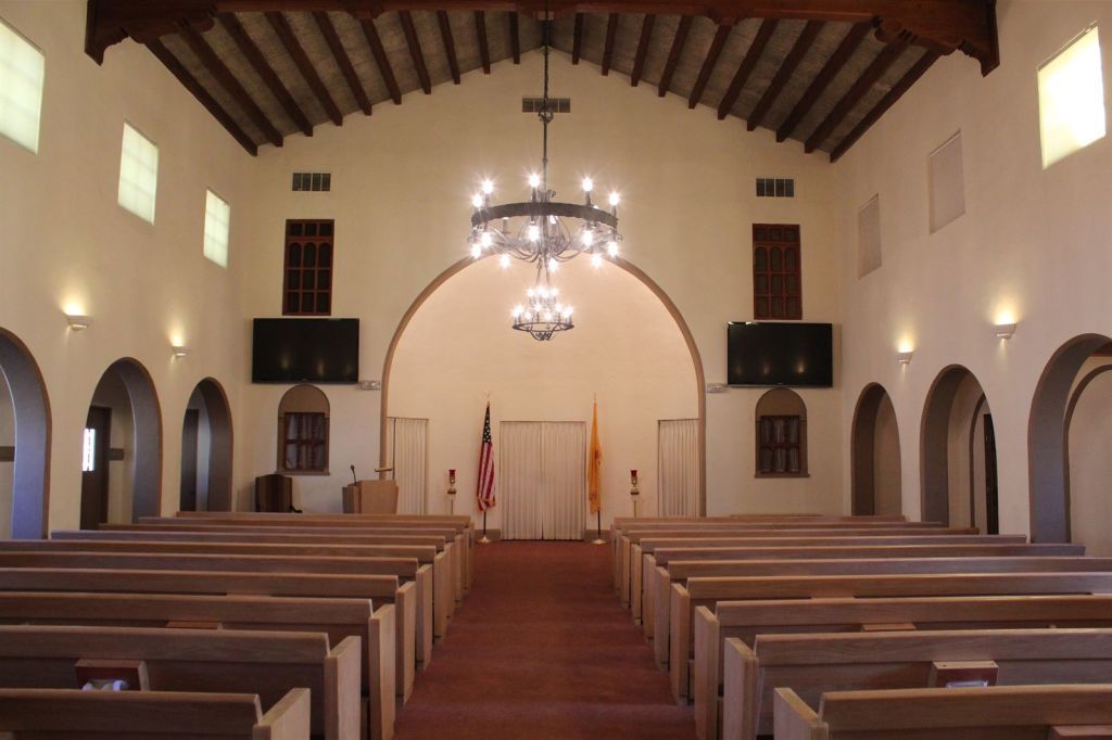 Interior of a church with rows of wooden pews, archways, and a chandelier hanging from the ceiling.