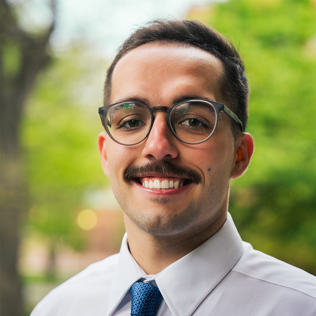 A man wearing glasses and a tie is smiling for the camera.